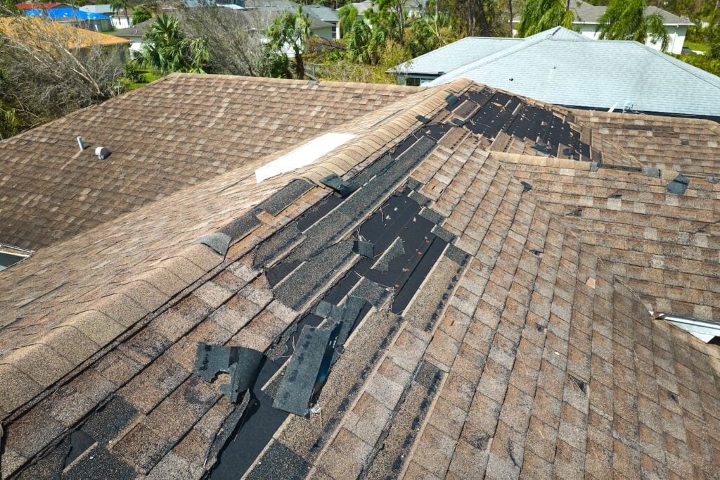 Damaged house roof with missing shingles after storm