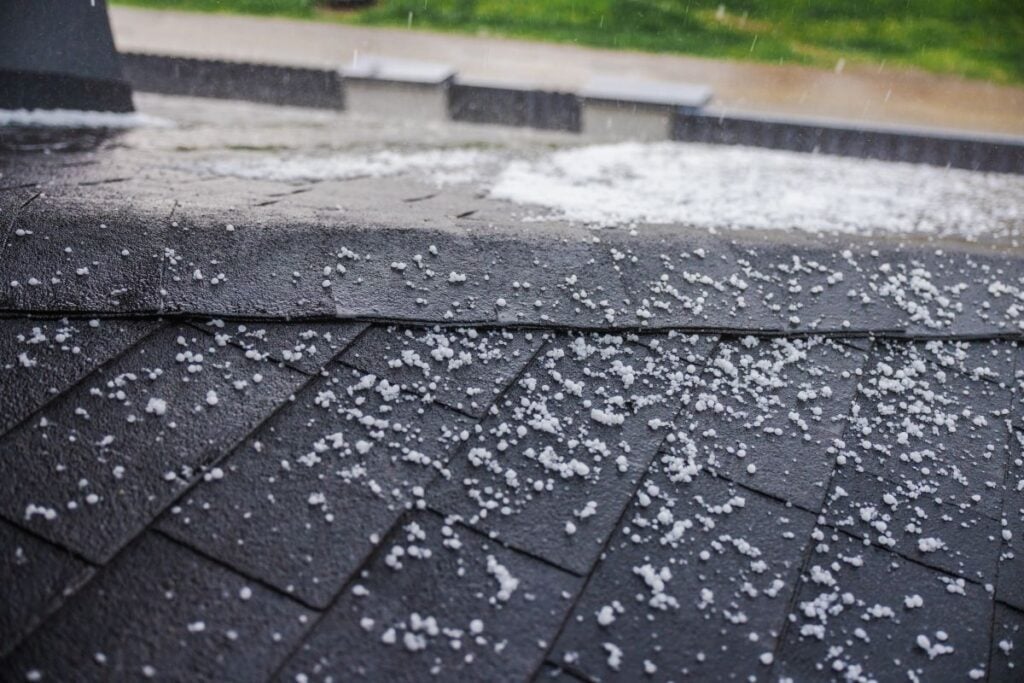 Small hailstones falling and covering a dark shingled roof during a rainstorm.