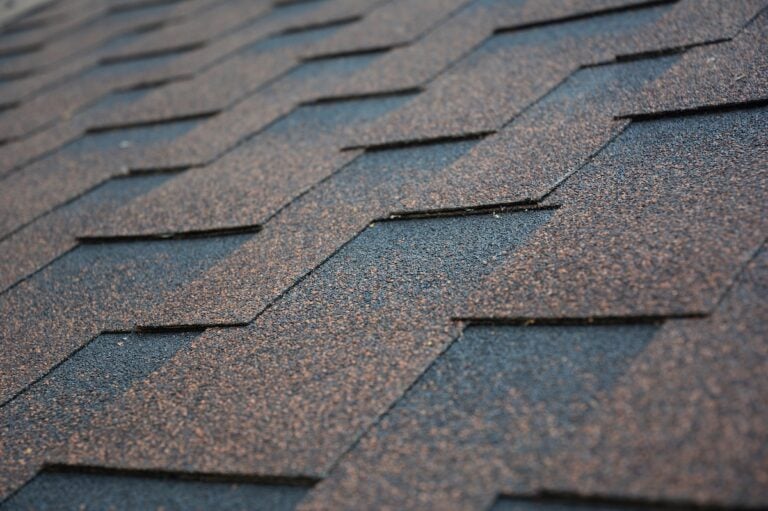 Copper, brown architectural, dimensional asphalt roofing shingles background. A close-up of a roof covered with brown asphalt shingles.