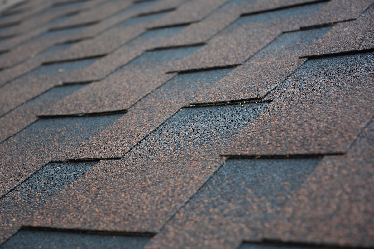 Copper, brown architectural, dimensional asphalt roofing shingles background. A close-up of a roof covered with brown asphalt shingles.