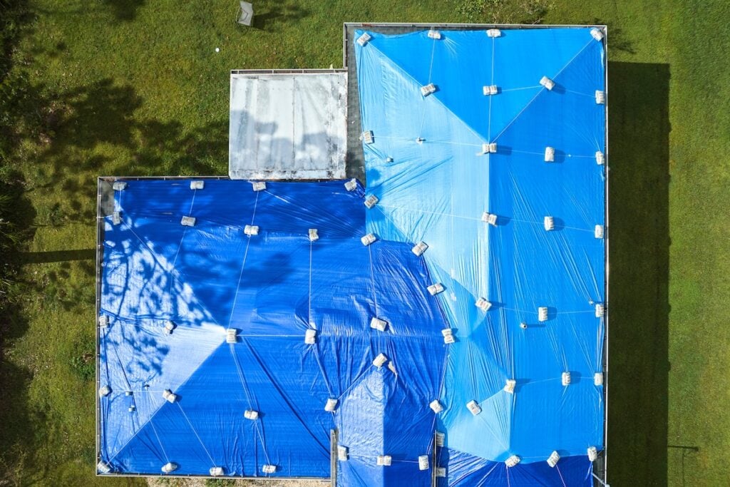 Top view of leaking house roof covered with protective tarp sheets against rain water leaks until replacement of asphalt shingles.