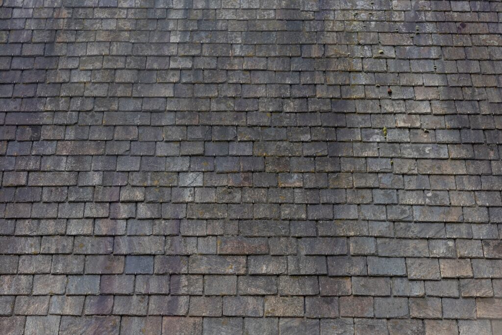 Old dark brown stone tiles covered with moss and rust stain on brick roof, Shingles texture, Abstract geometric pattern background, Details of roof top material.