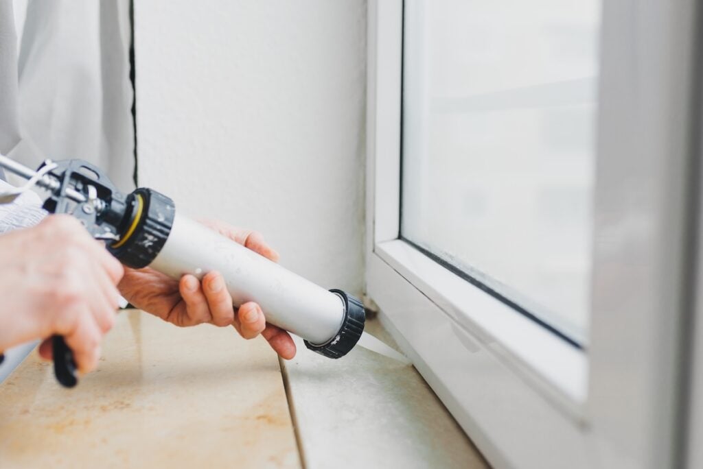 Hands of worker using a silicone tube for repairing of window