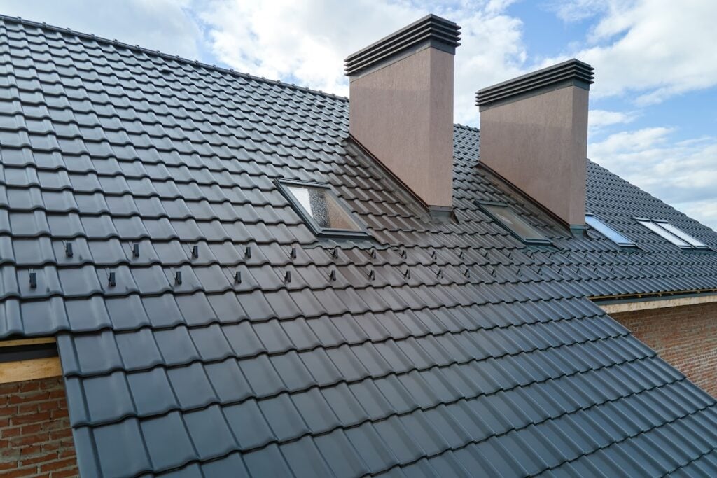 Closeup of attic windows and brick chimneys on house roof top covered with ceramic shingles.