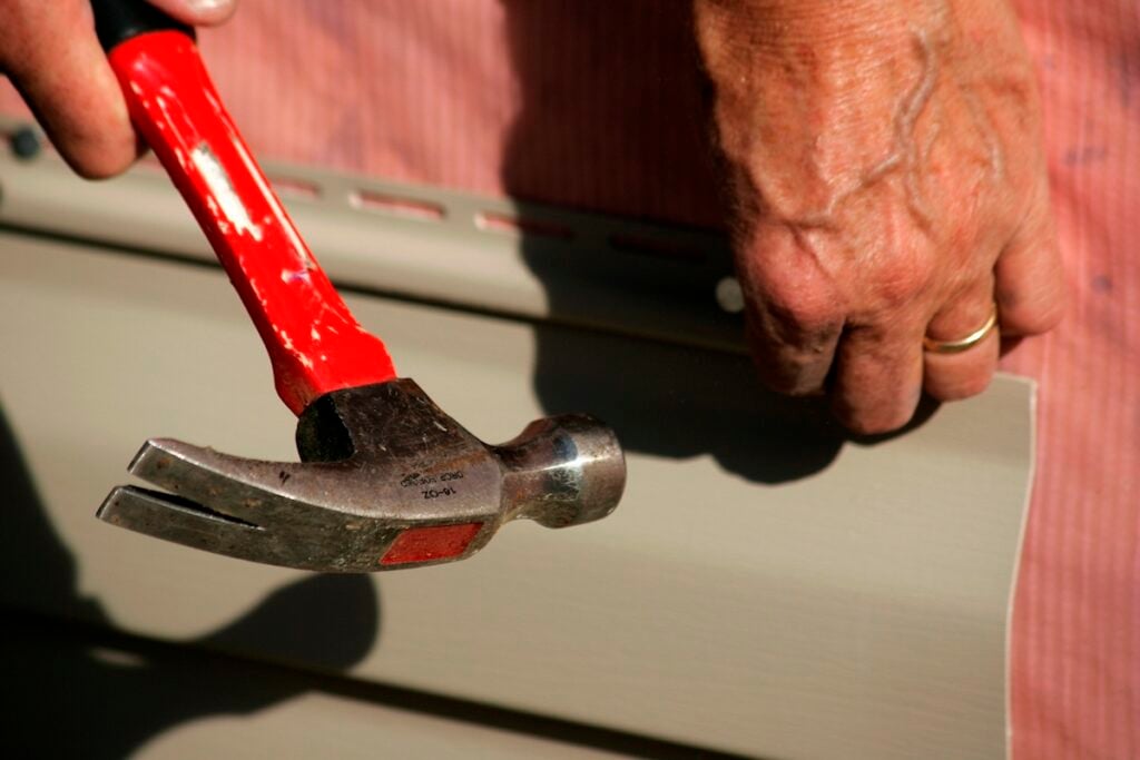 A pair if hands hammering a nail into vinyl siding